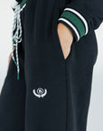 A model wearing a black sweatpant with green and white stripe details, paired with a matching sweatshirt.