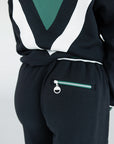 A model wearing a black sweatpant with green and white stripe details, paired with a matching sweatshirt.