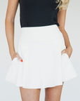 A woman wearing a white high-waisted skirt with built-in shorties and side seam pockets, paired with a black top.