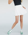 A woman wearing a white high-waisted skirt with built-in shorties and side seam pockets, paired with a black top.