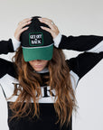 Black and green cap with 'GET OFF MY BACK' text worn by a model.