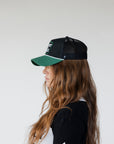 Black and green cap with 'GET OFF MY BACK' text worn by a model.