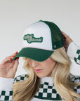 A woman wearing a white and green trucker hat with the text 'Golfing Optional' embroidered on the front.