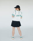 A person wearing a white golf shirt with green and black stripes, featuring a flamingo graphic and the text 'Fore All 04'. They are also wearing a black skirt and a black hat with text.