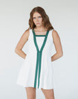 A female model wearing a white sleeveless knee-length dress with green accents and white sneakers.