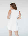 Woman wearing a white sleeveless dress against a plain background
