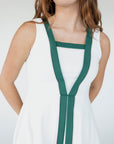 A female model wearing a white sleeveless knee-length dress with green accents and white sneakers.