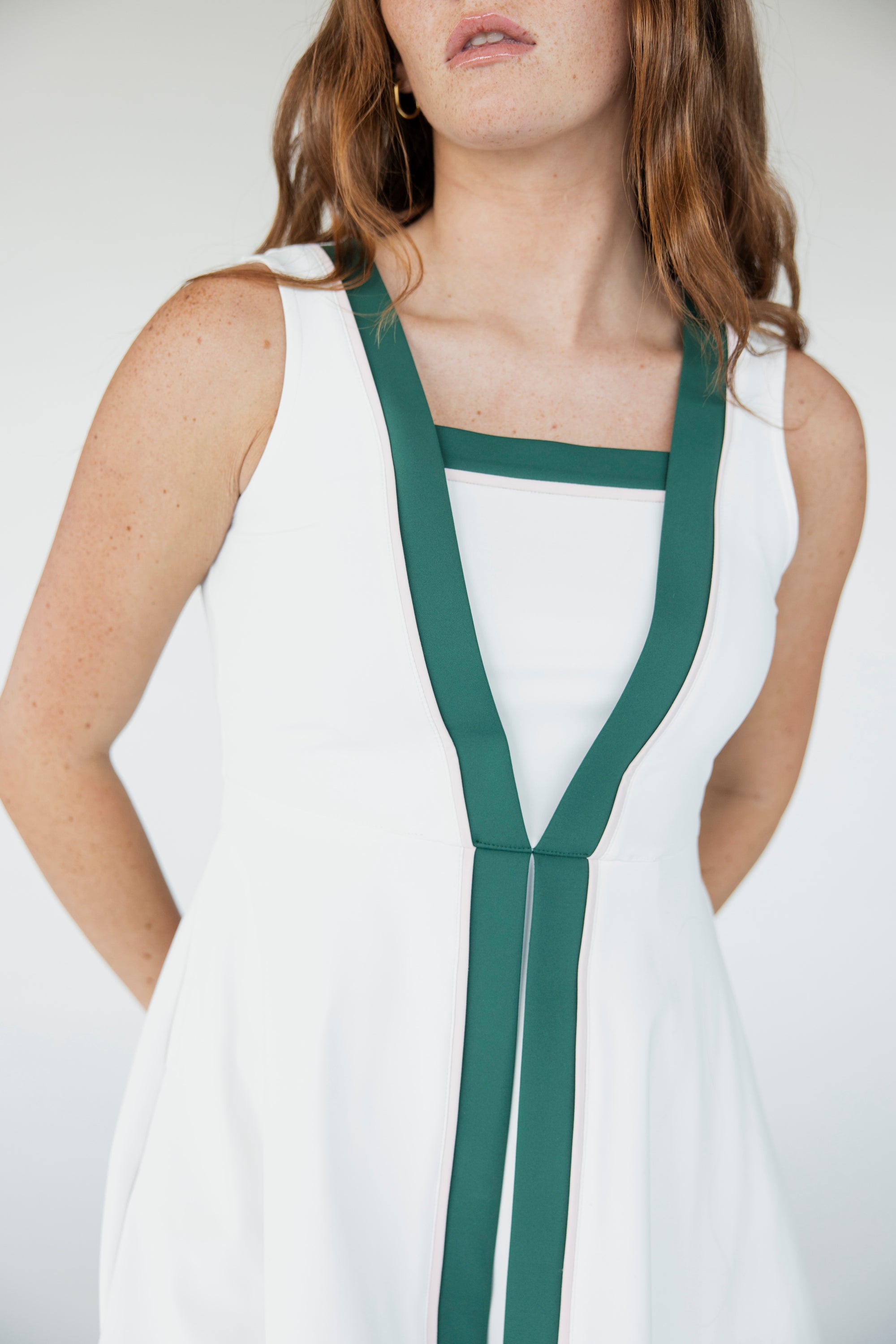 A female model wearing a white sleeveless knee-length dress with green accents and white sneakers.
