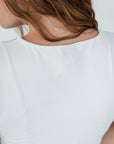 A female model wearing a white sleeveless knee-length dress with green accents and white sneakers.
