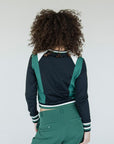 A female model wearing a black and green color-blocked crew neck golf shirt with long sleeves.