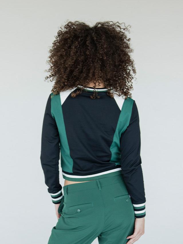 A female model wearing a black and green color-blocked crew neck golf shirt with long sleeves.