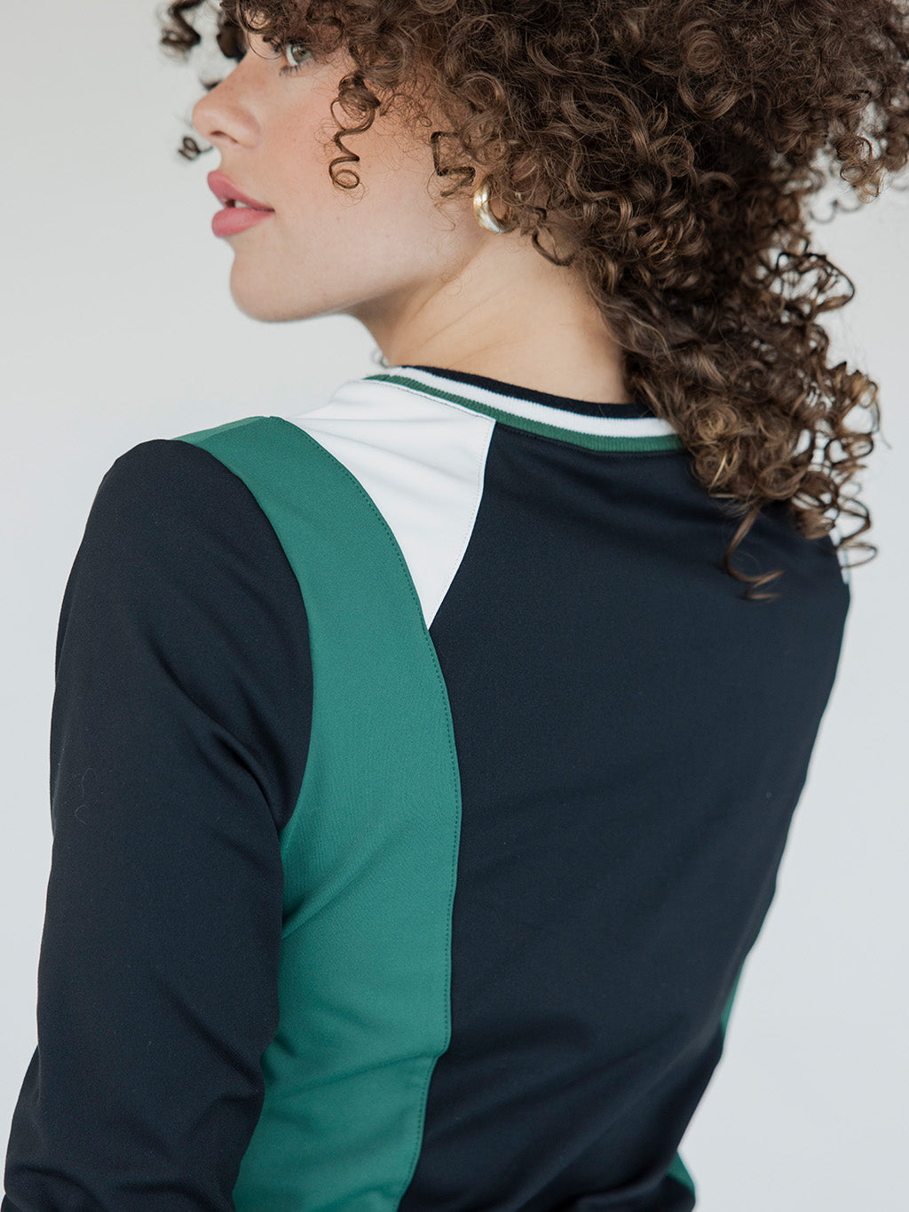 A female model wearing a black and green color-blocked crew neck golf shirt with long sleeves.