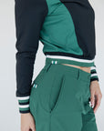 A female model wearing a black and green color-blocked crew neck golf shirt with long sleeves.
