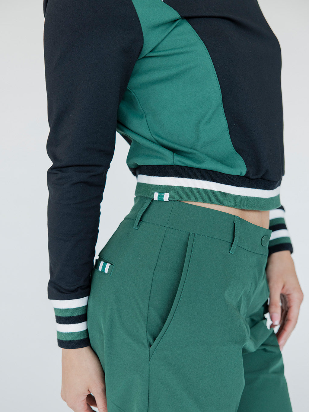 A female model wearing a black and green color-blocked crew neck golf shirt with long sleeves.