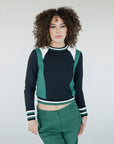 A woman wearing a black and green long-sleeved crew neck shirt with white stripes on the sleeves, paired with green pants.