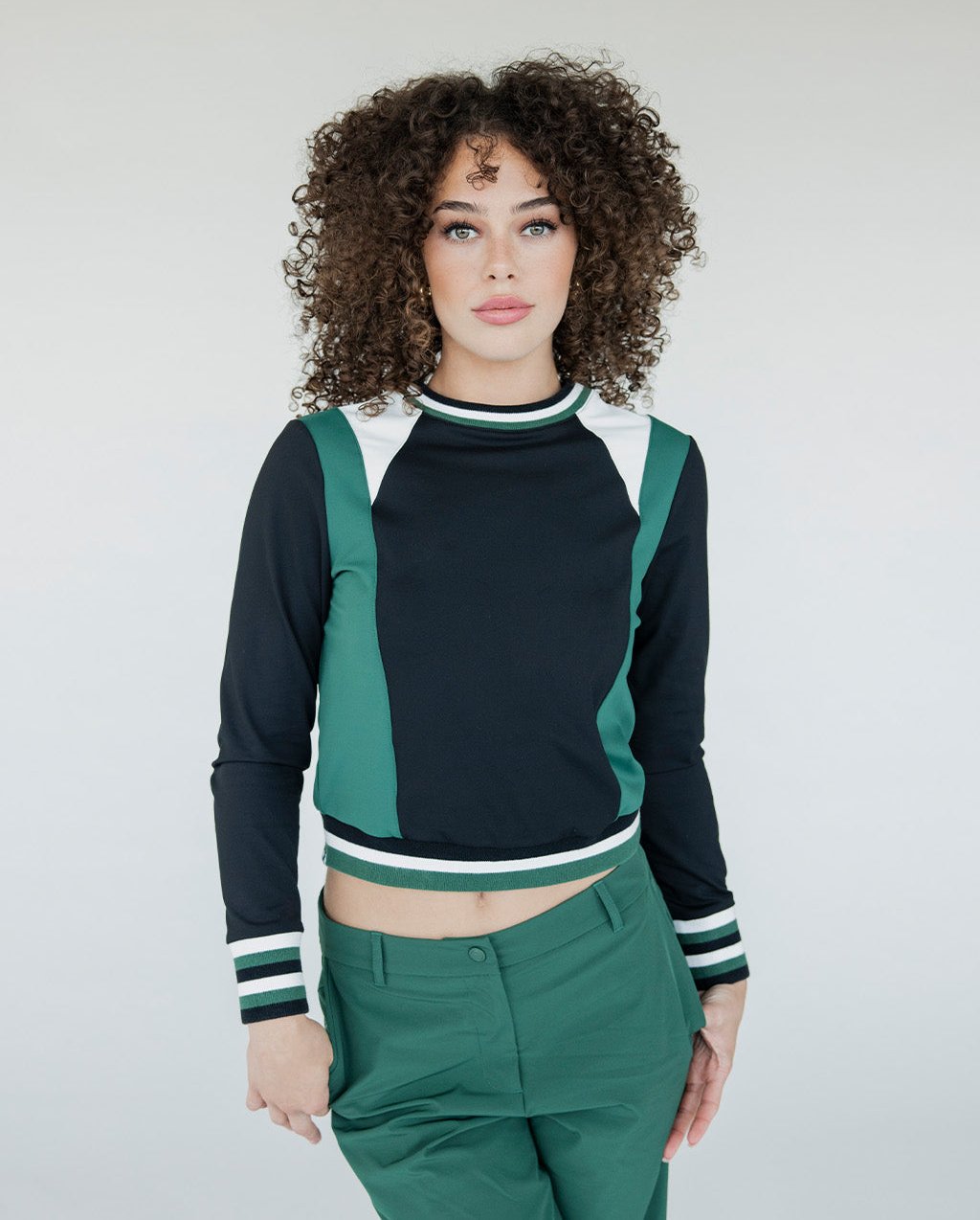 A woman wearing a black and green long-sleeved crew neck shirt with white stripes on the sleeves, paired with green pants.