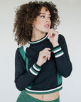 A female model wearing a black and green color-blocked crew neck golf shirt with long sleeves.