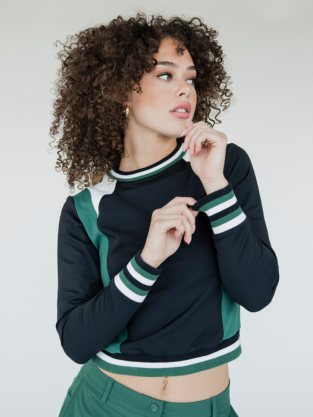A female model wearing a black and green color-blocked crew neck golf shirt with long sleeves.
