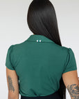 A woman wearing a green polo shirt with a collar, featuring a four-button placket and puff sleeves, paired with a black skirt.
