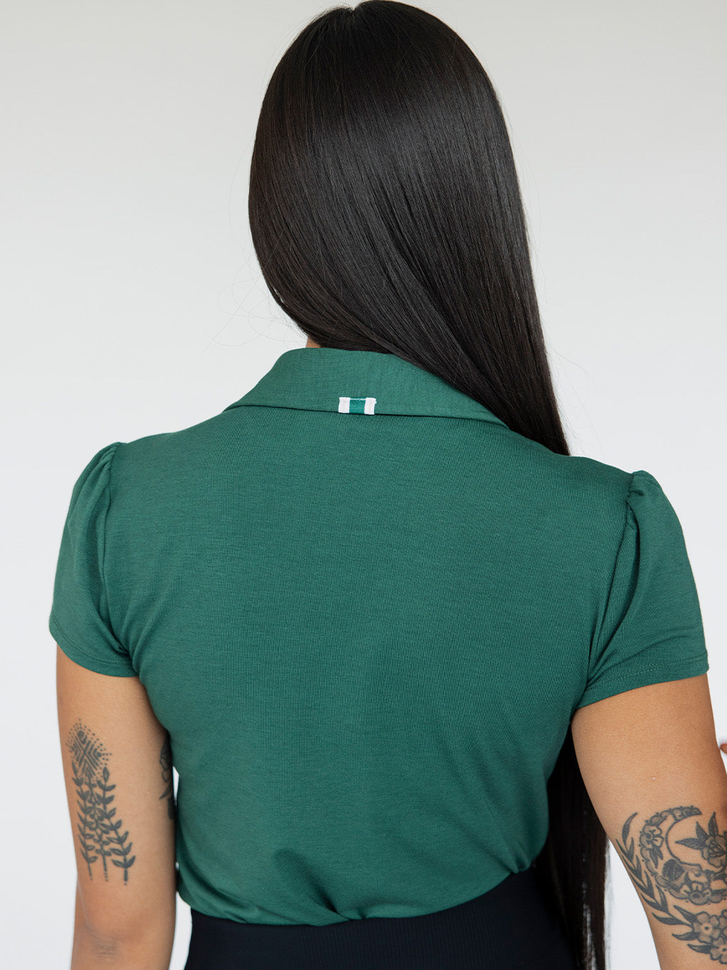 A woman wearing a green polo shirt with a collar, featuring a four-button placket and puff sleeves, paired with a black skirt.