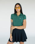 A woman wearing a green polo shirt with a collar, featuring a four-button placket and puff sleeves, paired with a black skirt.