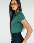 A woman wearing a green polo shirt with a collar, featuring a four-button placket and puff sleeves, paired with a black skirt.