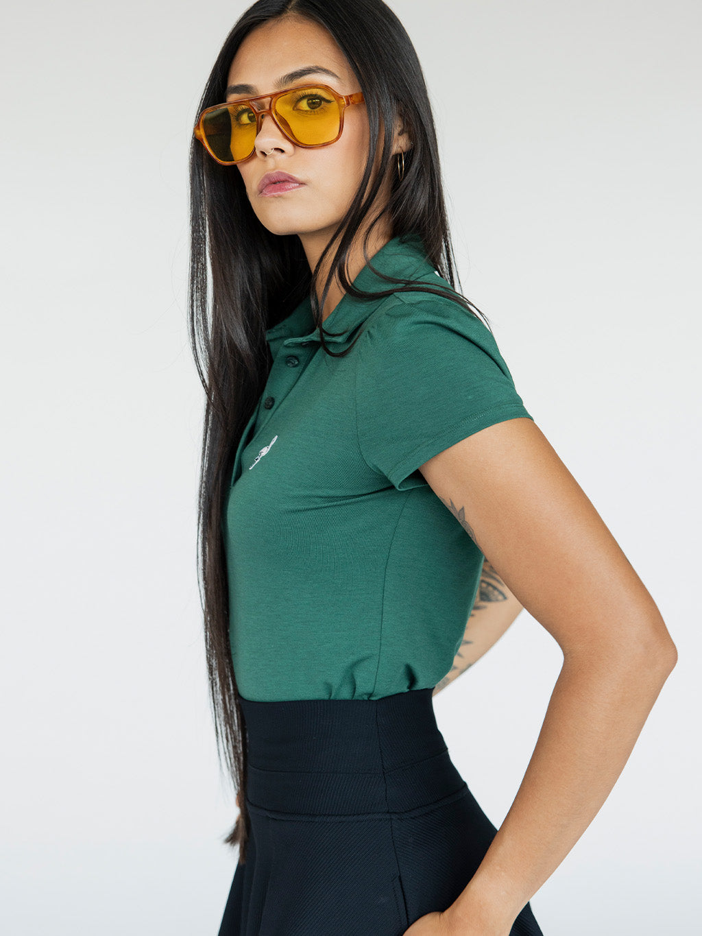A woman wearing a green polo shirt with a collar, featuring a four-button placket and puff sleeves, paired with a black skirt.