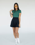 A woman wearing a green polo shirt with a collar, featuring a four-button placket and puff sleeves, paired with a black skirt.