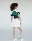 A woman wearing a white pleated golf skirt with a dark color waistband, paired with a gray top and white sneakers.