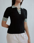 A woman wearing a black golf polo shirt with a geometric design on the collar and sleeves, and light pink pants.
stylish women’s golf top outfit.