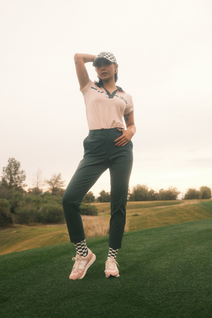 Pink Golf Pants with white pipping down the side of leg on her back with white golf shoes and golf socks with logo Fore All on sock 