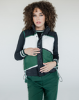 A female model wearing a color-blocked puffer vest in green, black, and white, paired with green pants.