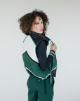 A female model wearing a color-blocked puffer vest in green, black, and white, paired with green pants.
