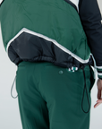 A female model wearing a color-blocked puffer vest in green, black, and white, paired with green pants.