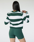 A woman wearing a green and white striped sweater with a V-neck collar and a small embroidered logo on the chest.