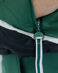 A female model wearing a color-blocked puffer vest in green, black, and white, paired with green pants.