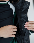 A female model wearing a color-blocked puffer vest in green, black, and white, paired with green pants.