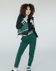 A female model wearing a color-blocked puffer vest in green, black, and white, paired with green pants.