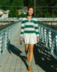 A woman wearing a green and white striped sweater with a V-neck collar and a small embroidered logo on the chest.