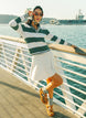 A woman wearing a green and white striped sweater with a V-neck collar and a small embroidered logo on the chest.