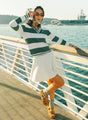 A woman wearing a green and white striped sweater with a V-neck collar and a small embroidered logo on the chest.