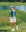 Woman on a golf course with a lake in the background wearing a green and white color-blocked crew neck golf shirt with long sleeves.