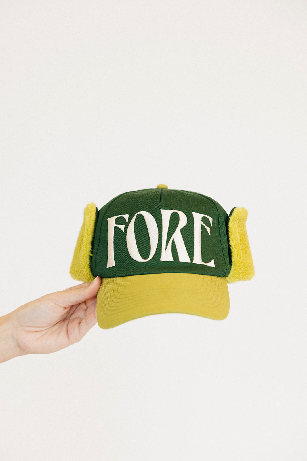 Green and yellow cap with 'FORE' text held by a hand on a white background