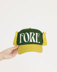 Green and yellow cap with 'FORE' text held by a hand on a white background