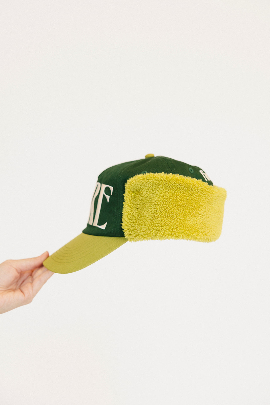 Green and avocado cap with 'FORE' text held by a hand on a white background