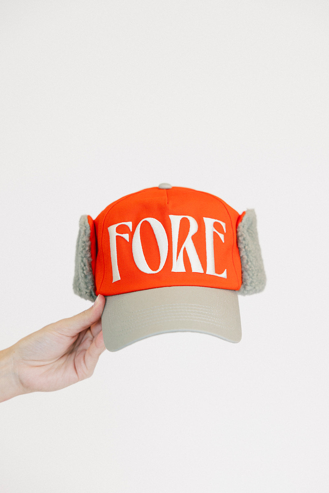 Person holding an red cap and a white sweatshirt with red text on a light background