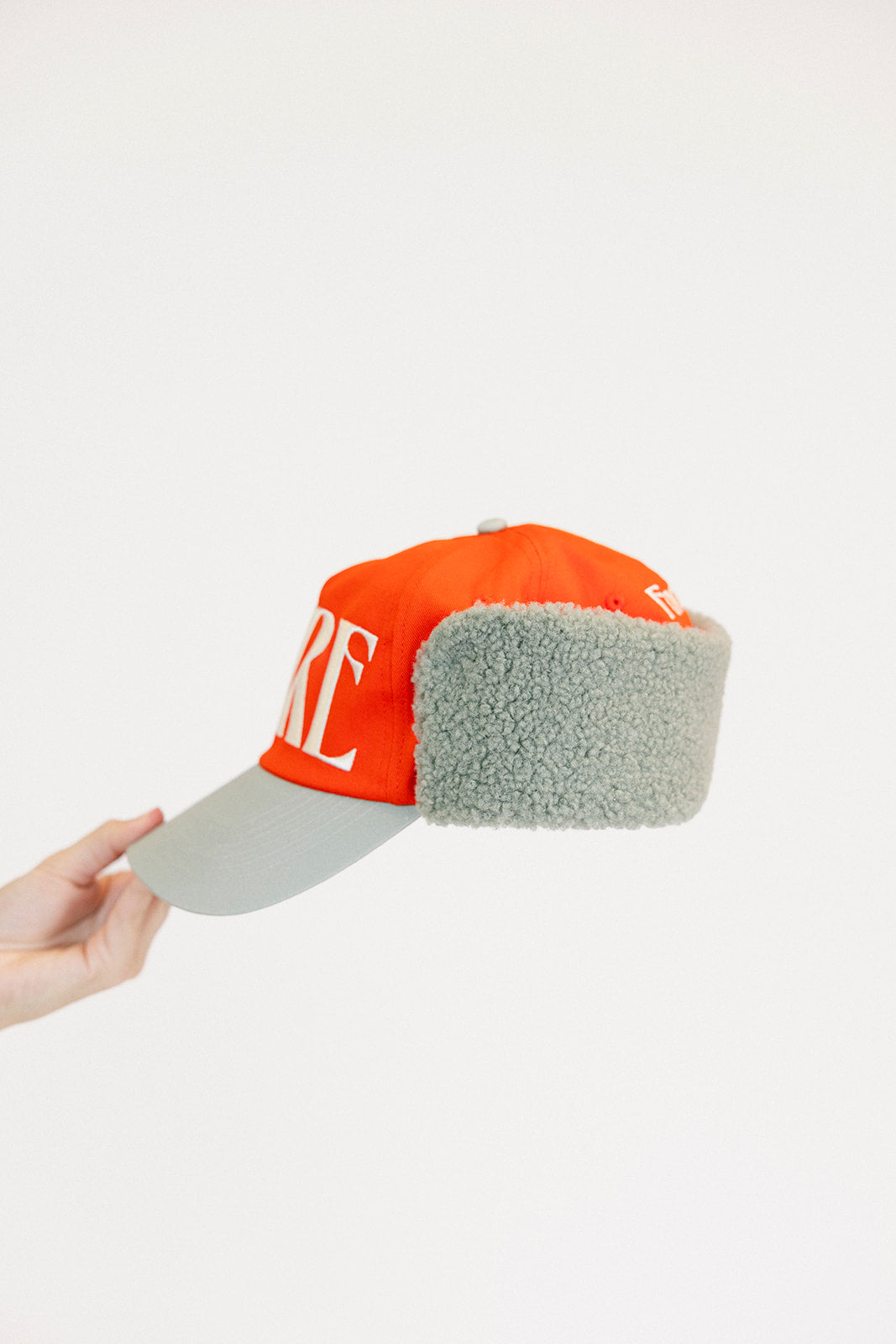 Person holding an red cap and a white sweatshirt with red text on a light background