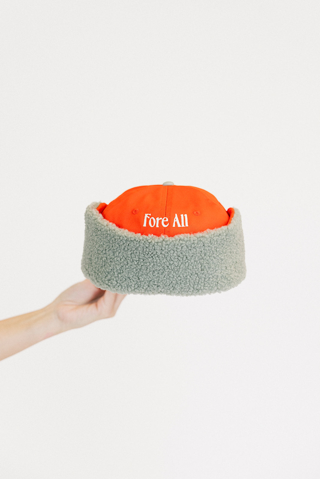 Person holding an red cap and a white sweatshirt with red text on a light background