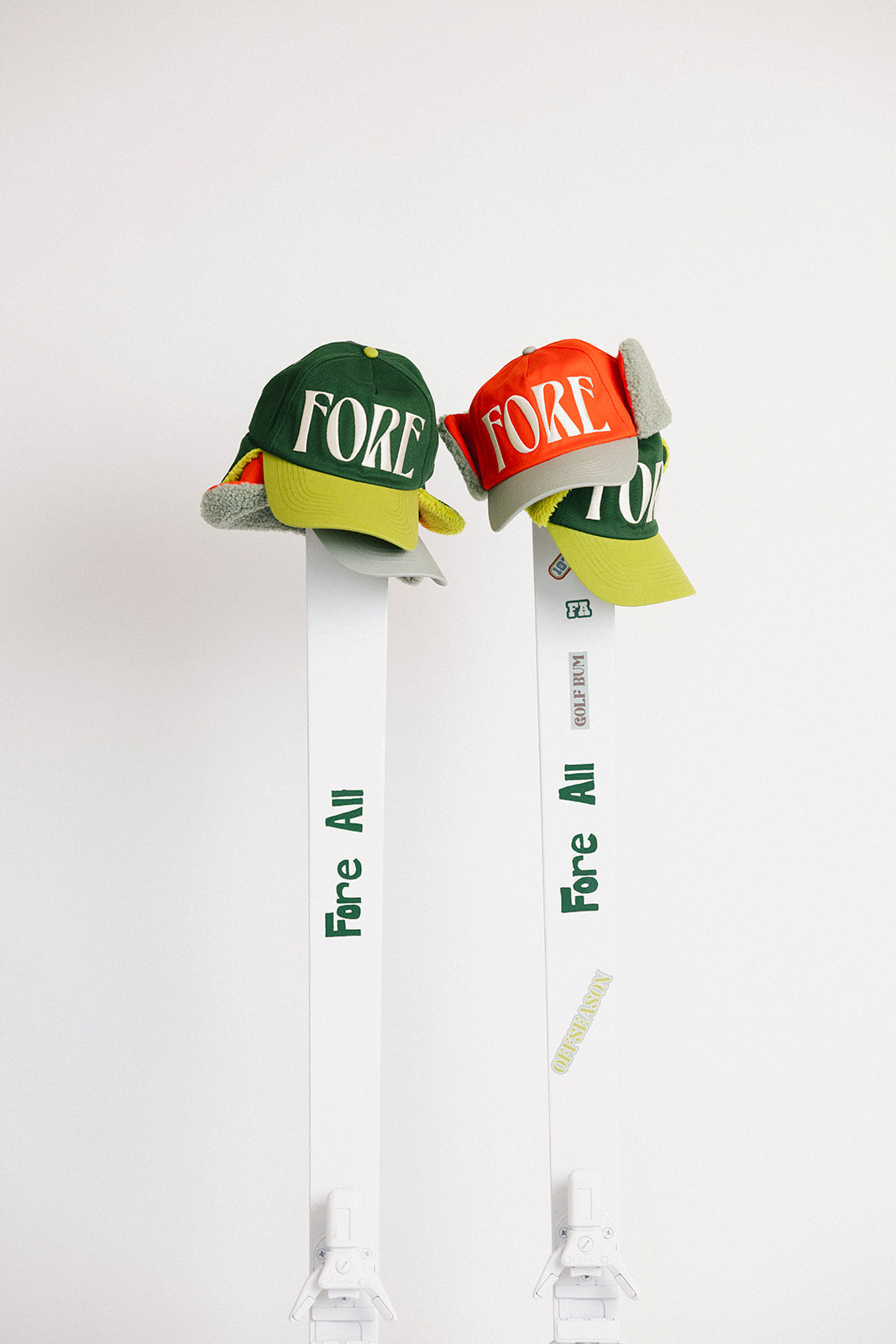 Two hats with &#39;FORE&#39; text hanging on skis on a white background