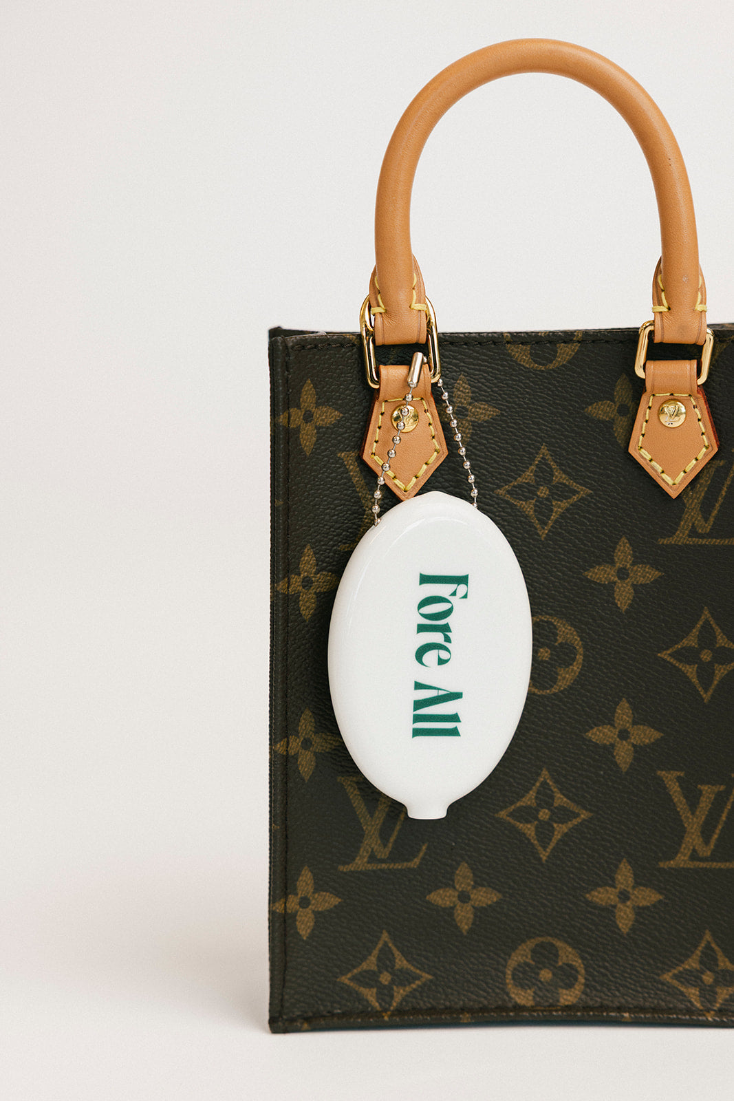 Louis Vuitton handbag with a white 'Fore All' golf ball holder attached